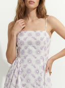 Woman wearing a white dress with purple floral pattern on a plain background
